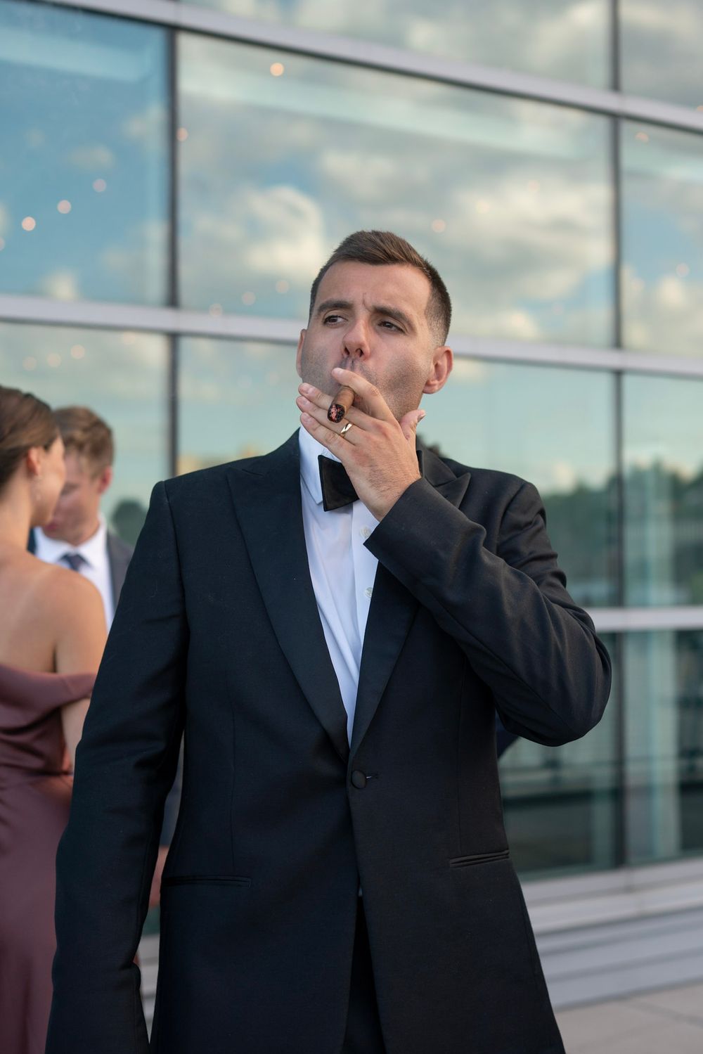 Sophisticated man in tuxedo exhaling cigar smoke at evening event.