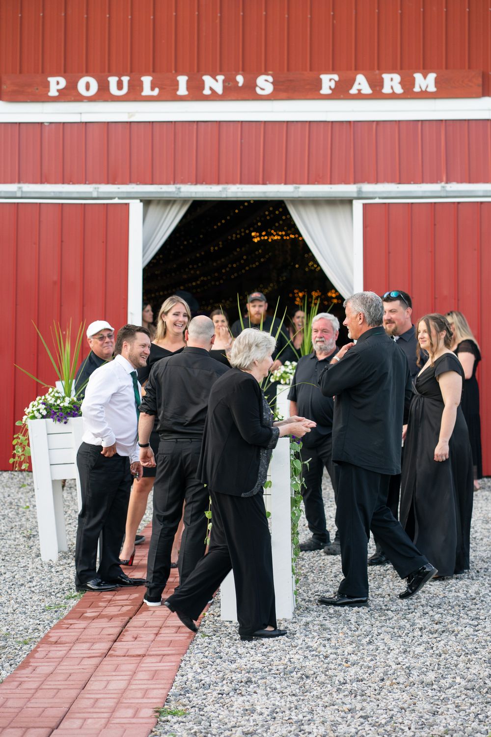 Wedding guests gather outside Poulin's Farm red barn venue decorated with white floral arrangements.