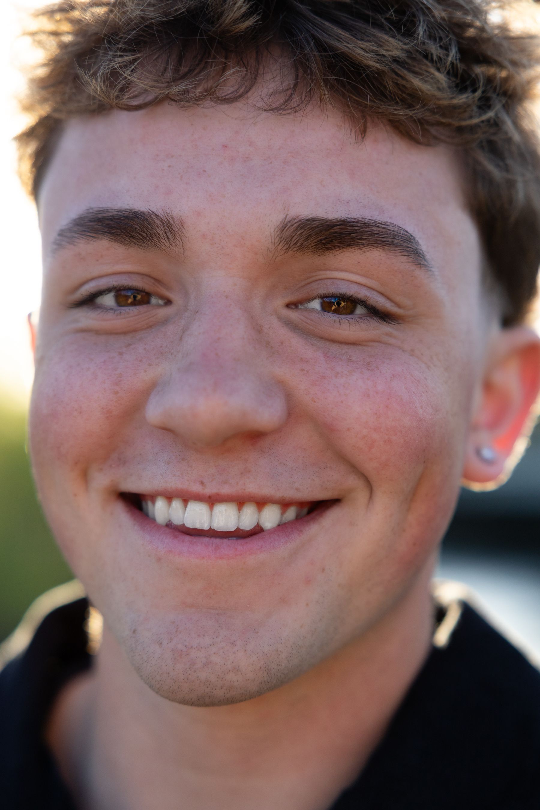 Close-up portrait of smiling young man with freckles and brown eyes outdoors.