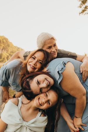 Three generations of women smiling and hugging outdoors in warm natural light.