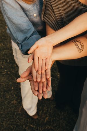 Close-up of three people stacking hands together outdoors, one with a small tattoo on their wrist.