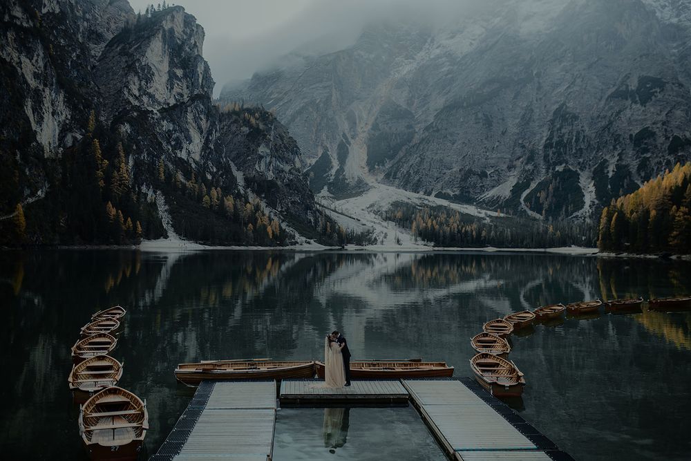 Misty alpine lake with wooden dock, rowboats, and dramatic mountain reflections at Lago di Braies, Italy.