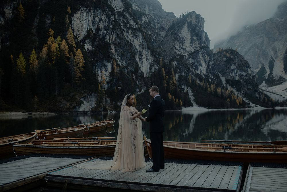 Couple exchanges vows on a dock at Lago di Braies, Dolomites, surrounded by wooden boats and misty mountain reflections.