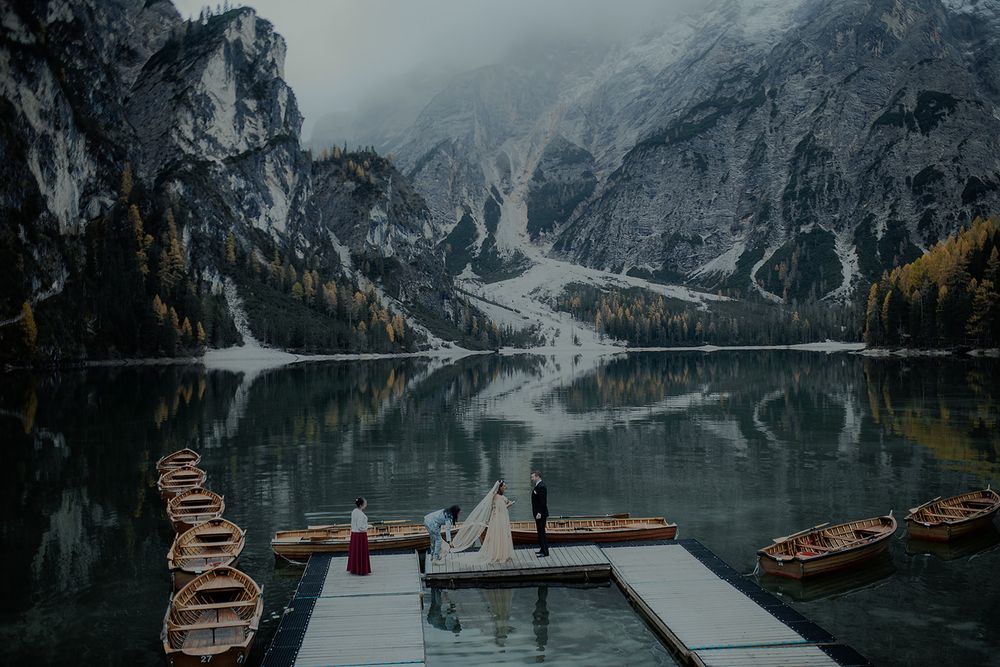 Couple eloping at Lago di Braies, Italy, with wooden boats and dramatic snow-capped Dolomites reflected in calm water.