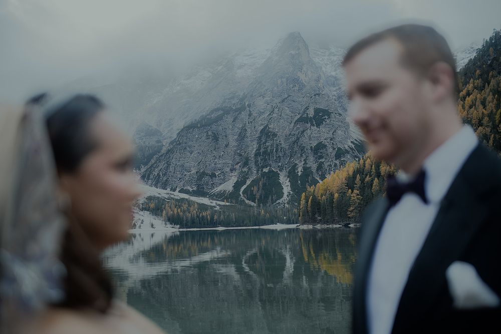 Couple in wedding attire with stunning mountain lake reflection at Lago di Braies, Dolomites, Italy.