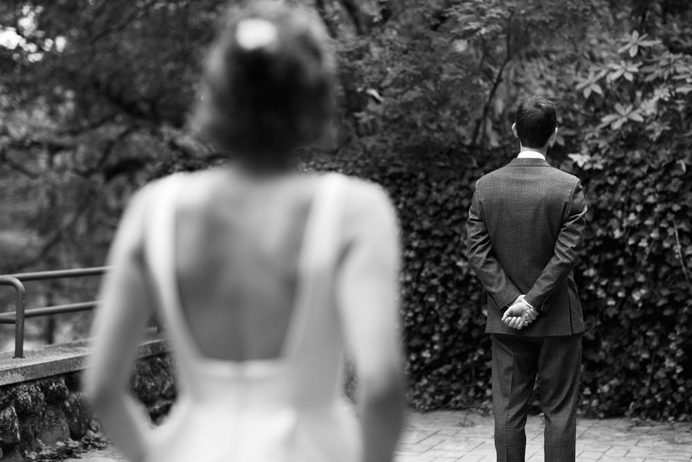 Black and white photo of bride approaching groom from behind during a wedding first look ceremony outdoors.
