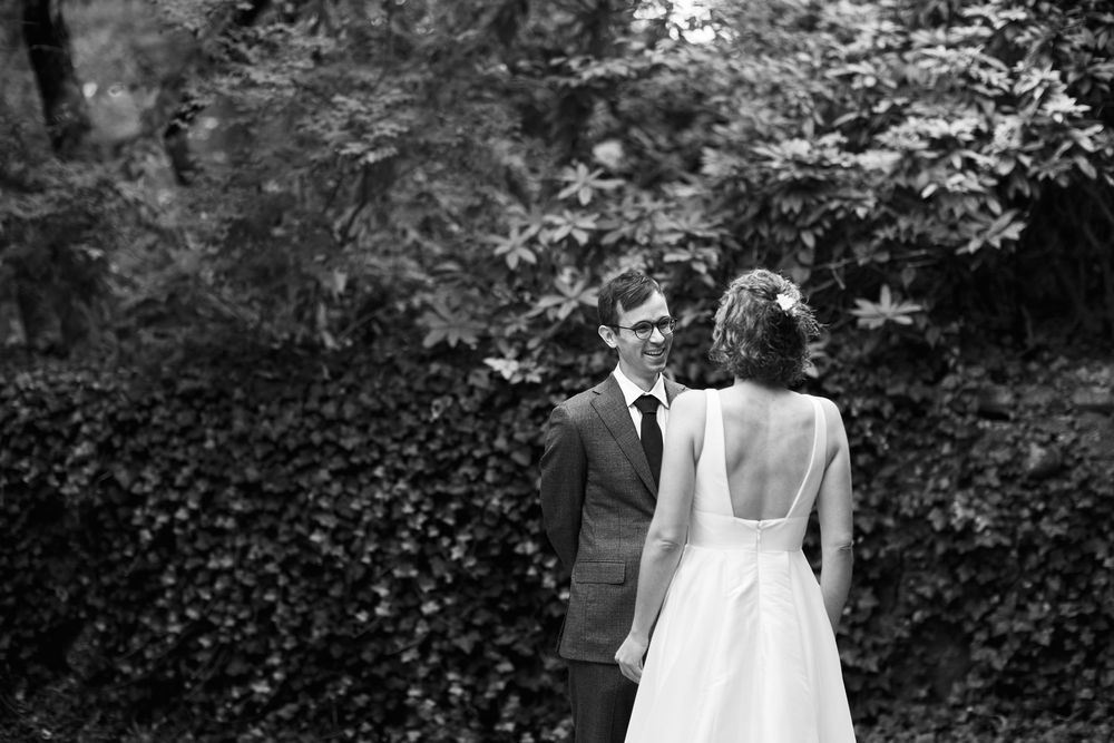 Black and white photo of a bride and groom facing each other in a lush garden setting.
