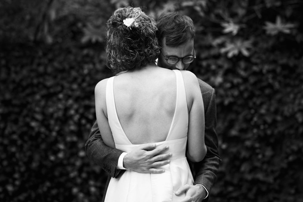 Black and white photo of a bride and groom embracing outdoors, showing the open back of her wedding dress.