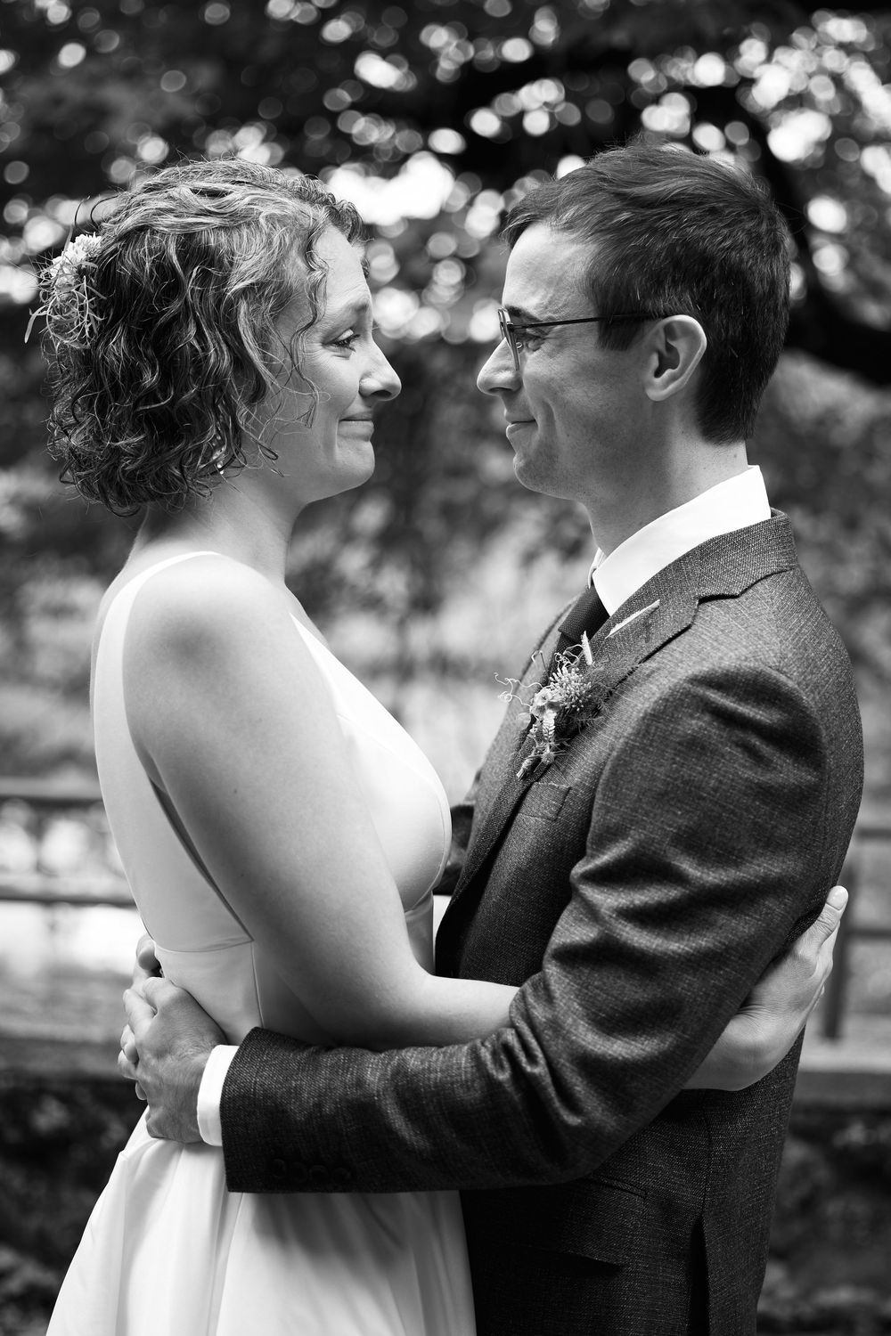 Black and white photo of a smiling bride and groom embracing outdoors on their wedding day.