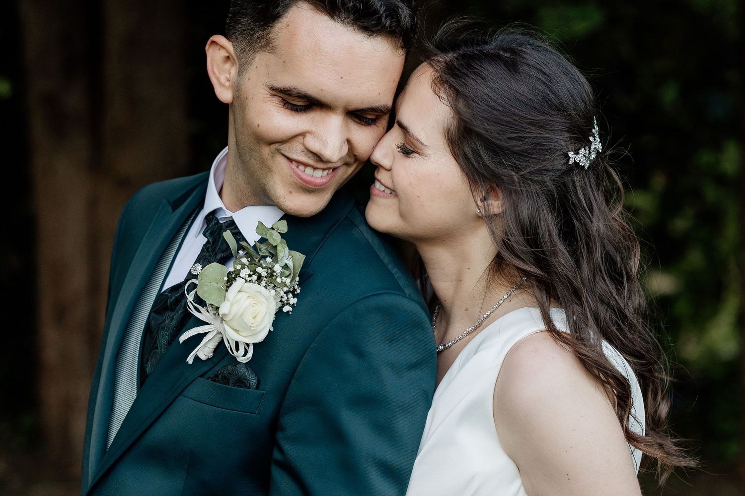 Newlywed couple shares a romantic moment against a white wall with blue trim, casting shadows in golden sunlight.
