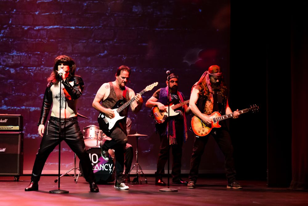 Rock band performs on stage with electric guitars and a female lead vocalist in black leather outfit.