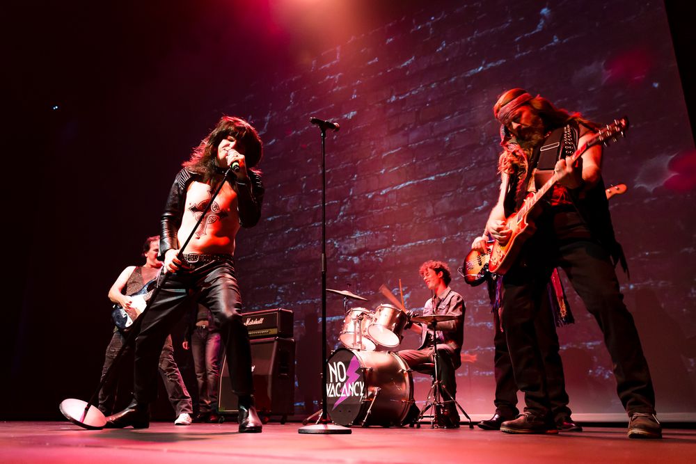 Rock band performs energetically on stage with electric guitars and dramatic red lighting.