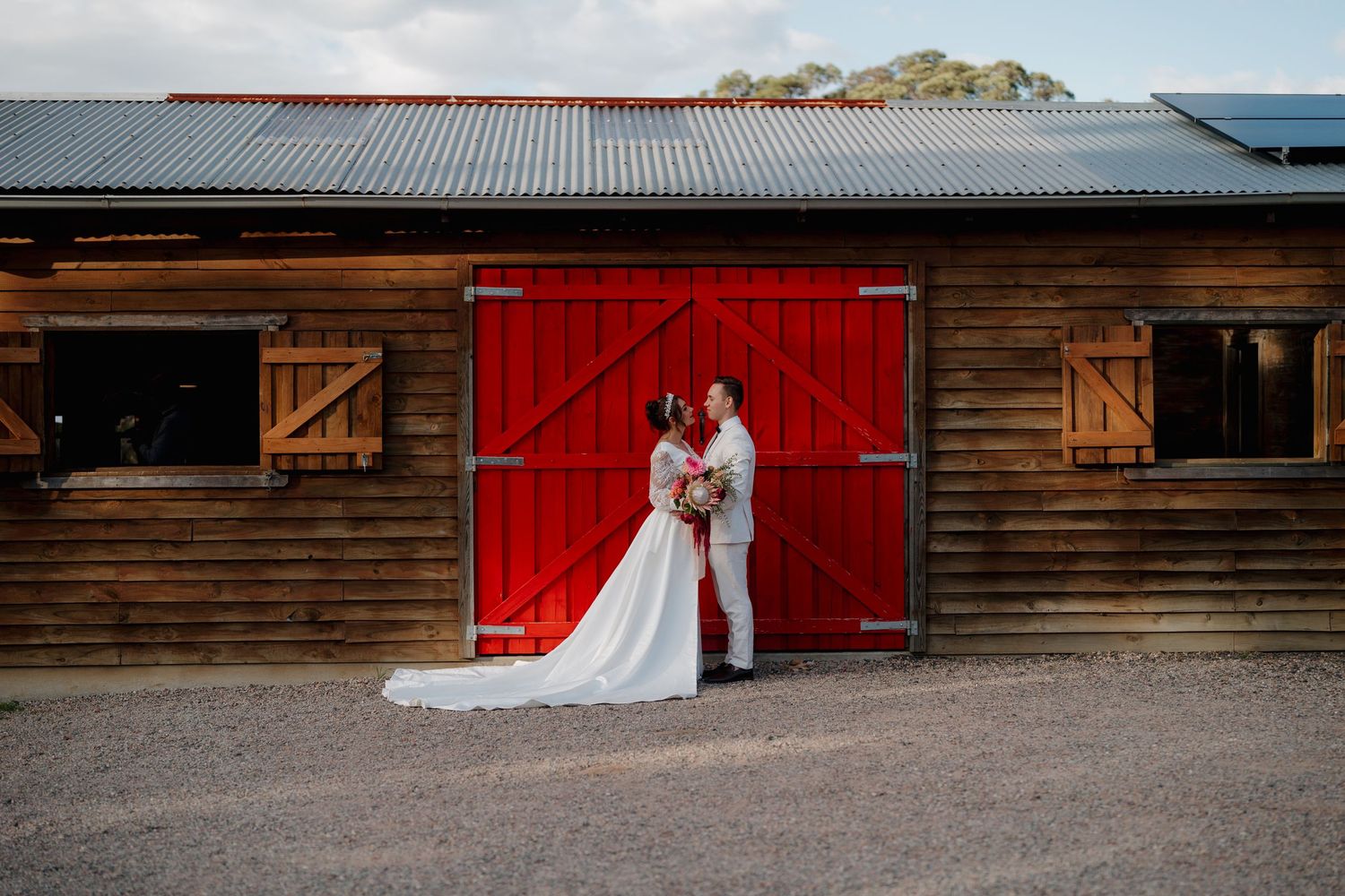 Bride and groom kissing in front of a rustic red barn door on their wedding day.