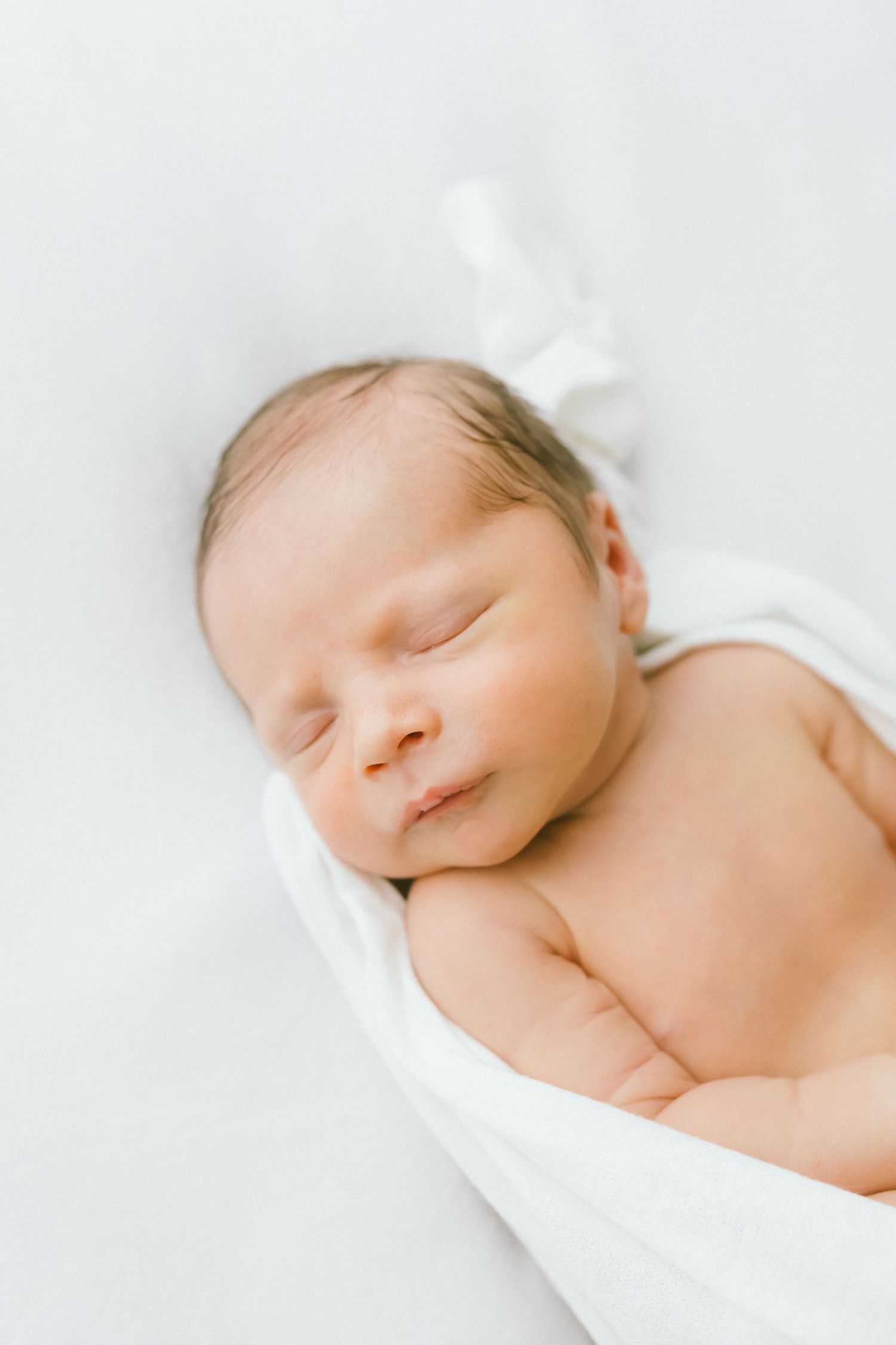 Peaceful newborn baby sleeping wrapped in a soft white swaddle blanket on a white background.