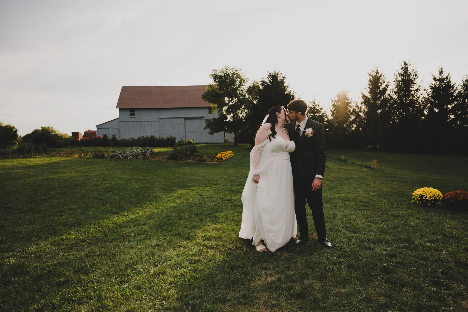 A couple walks through a scenic green field during sunset at their outdoor wedding celebration.
