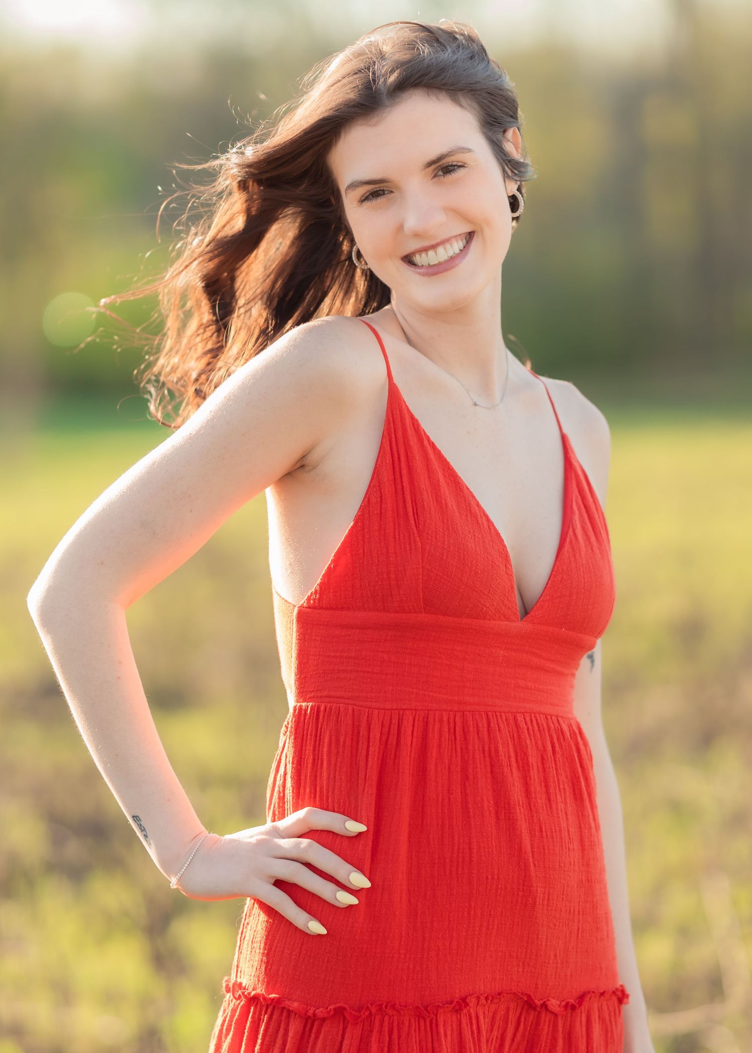 Young woman smiling in a red sundress outdoors at golden hour.