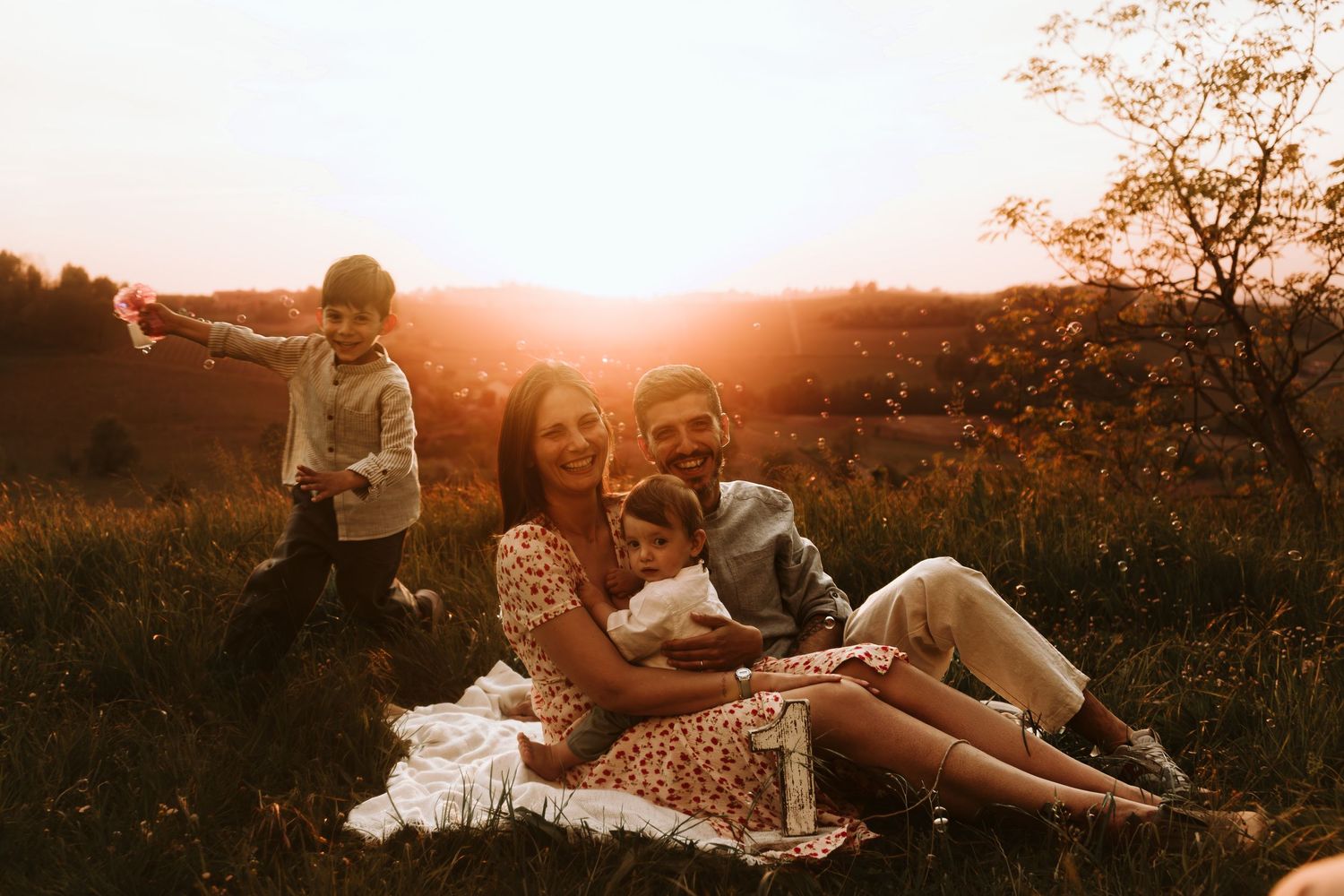 Family enjoying a golden sunset picnic in a meadow, with children playing and parents sitting on a blanket.