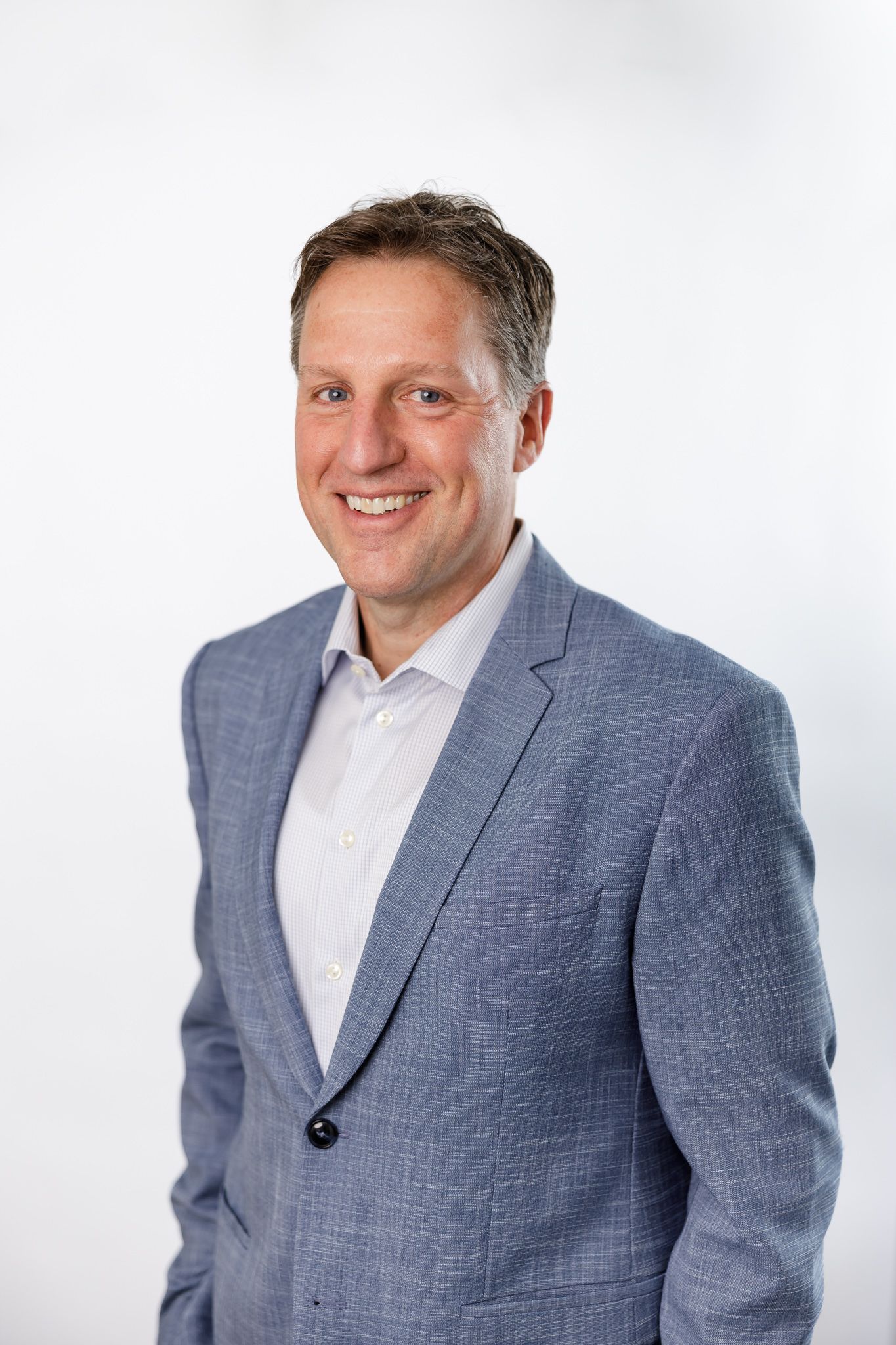 male real estate agent in Seattle, WA headshot on white background wearing blue suit smiling at camera