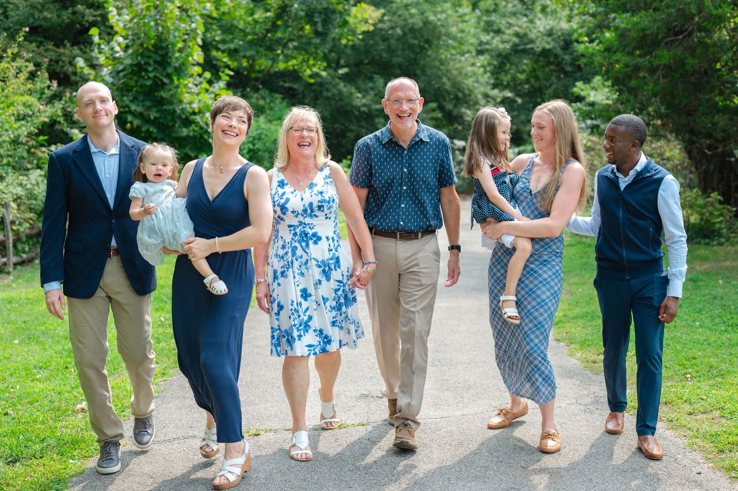 Multi-generational family group portrait smiling outdoors near a river, dressed in navy and blue attire in Long Island.