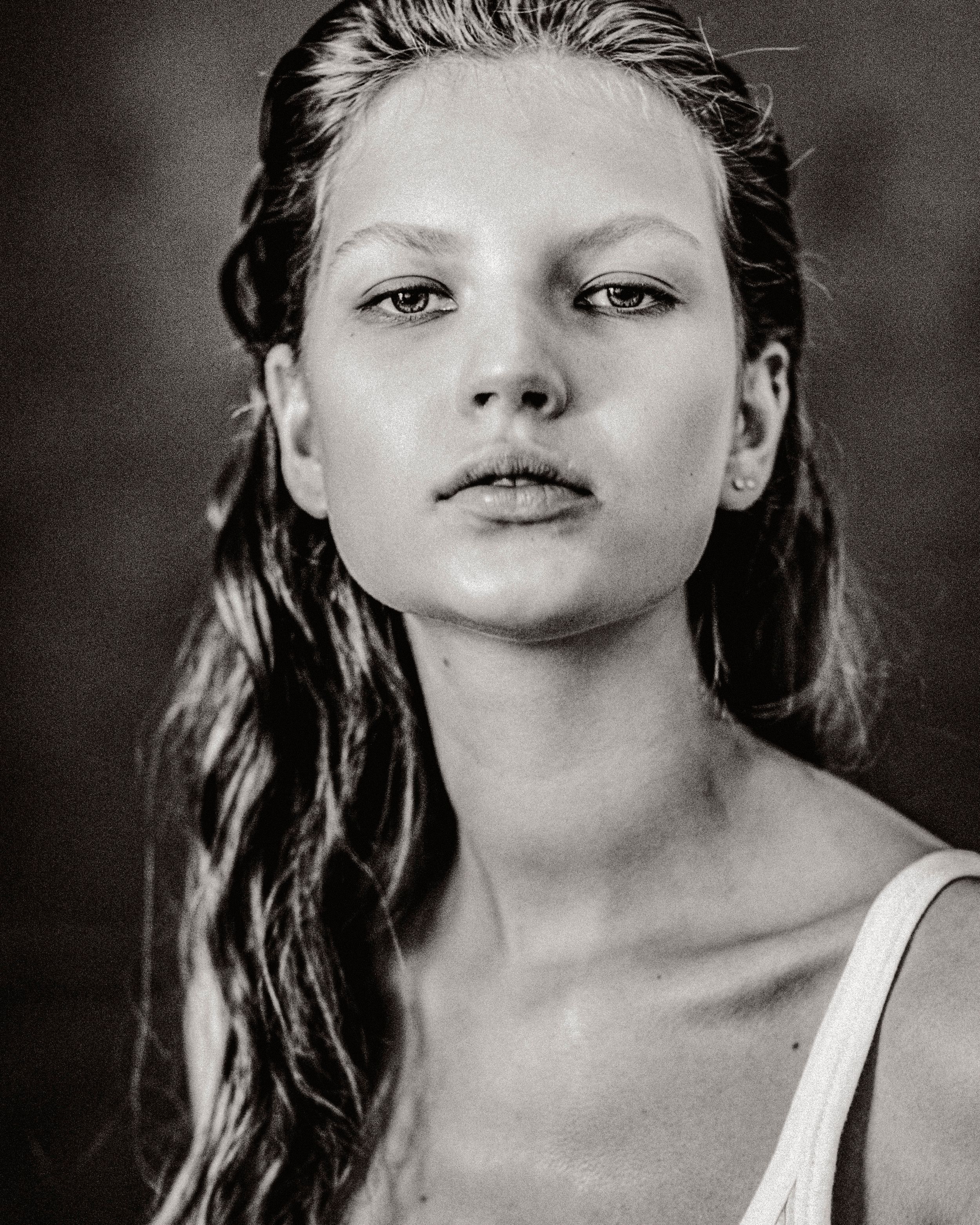 Black and white portrait of a young woman with wet hair wearing a white top, gazing directly at the camera.