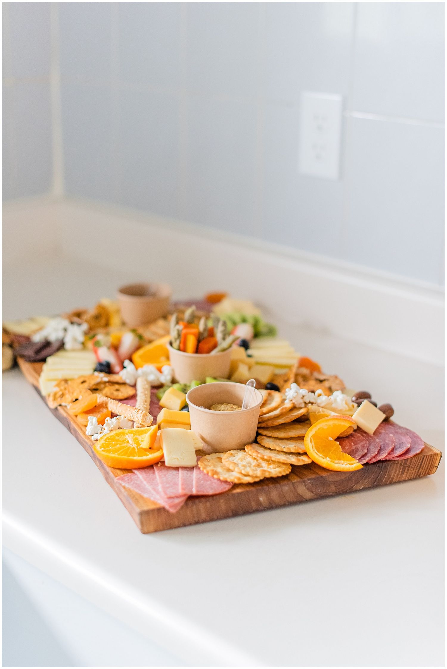 A beautifully arranged charcuterie board with cheese, crackers, meats, oranges, and dips on a wooden serving board.