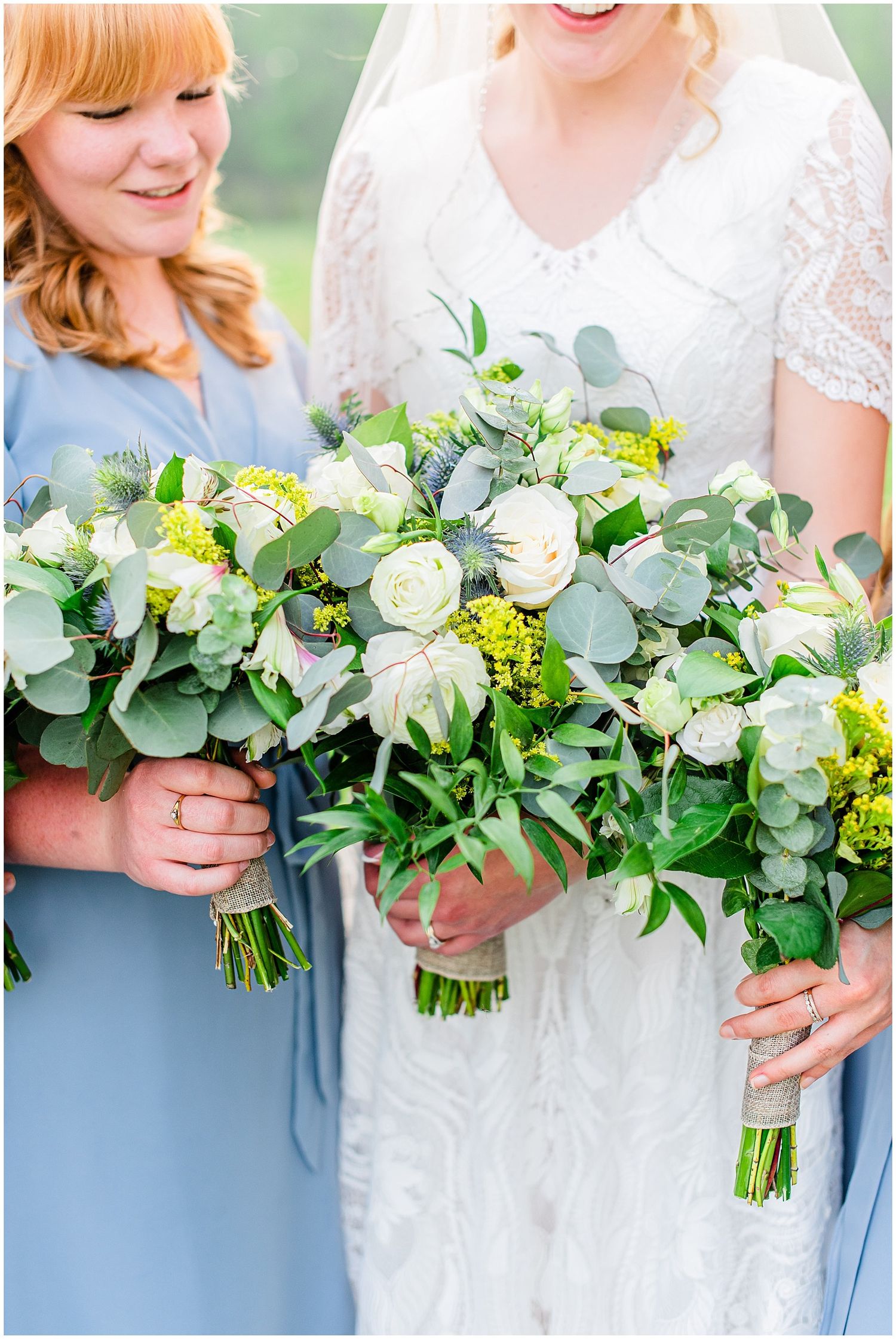 Bride and bridesmaid holding lush green and white wedding bouquets with eucalyptus in dusty blue dresses.