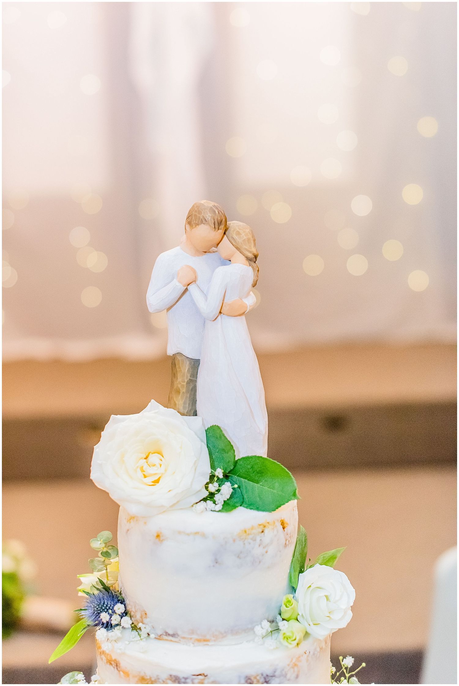 Elegant wedding cake topped with Willow Tree couple figurine and white roses with greenery accents.