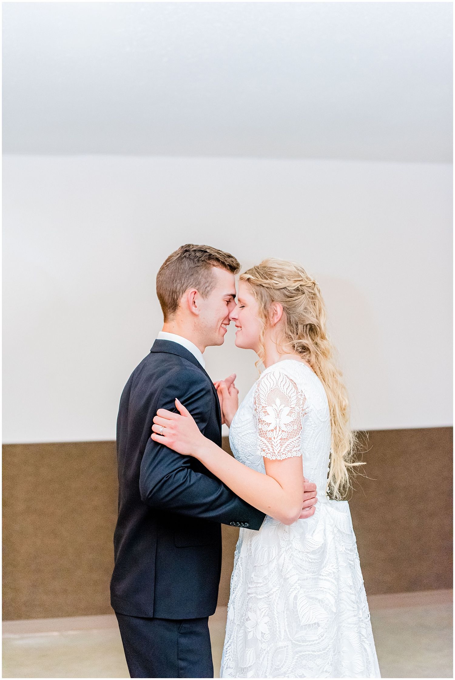 Bride and groom share romantic first dance moment in lace wedding dress and dark suit.
