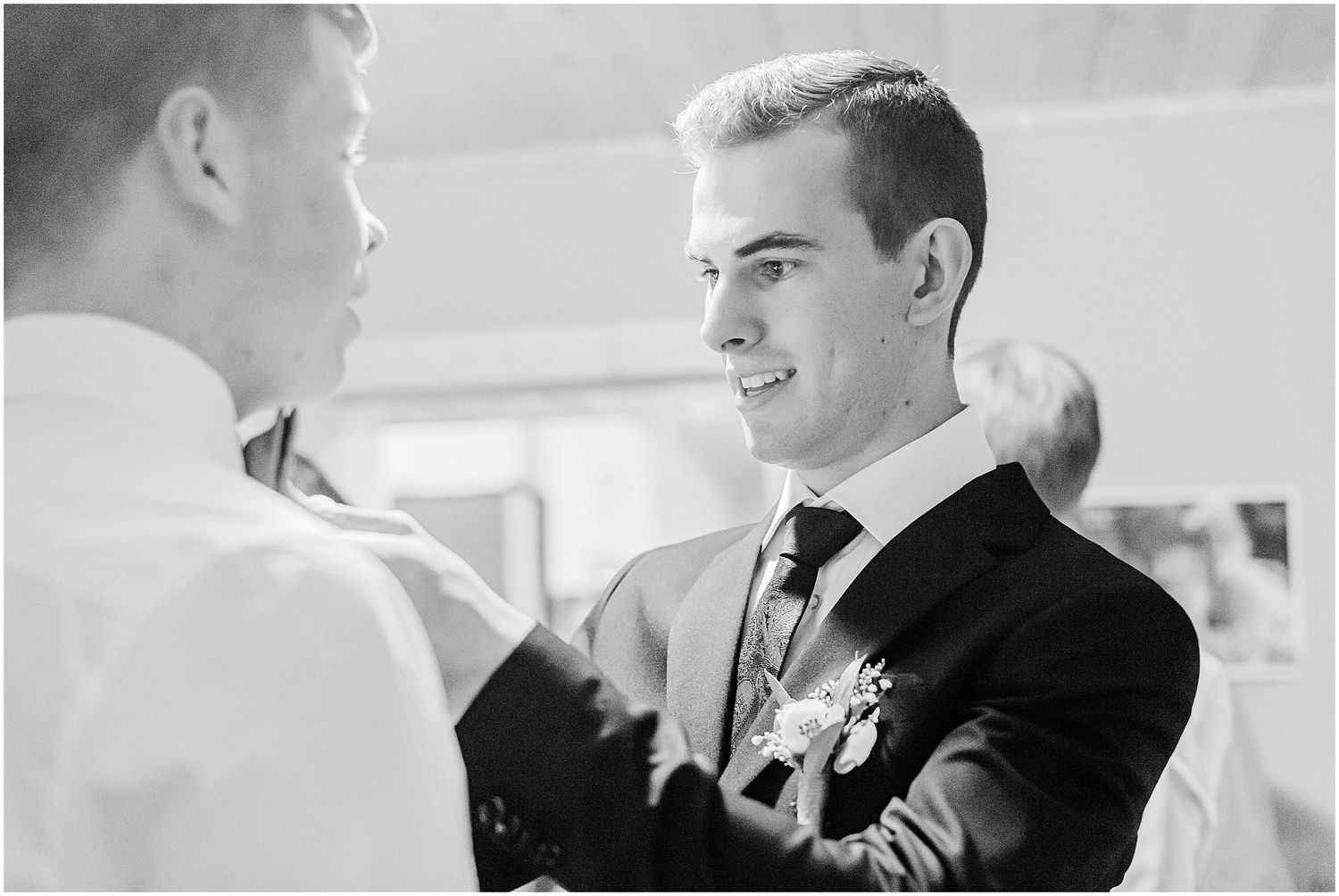 Black and white photo of two grooms sharing a tender moment during wedding preparations.