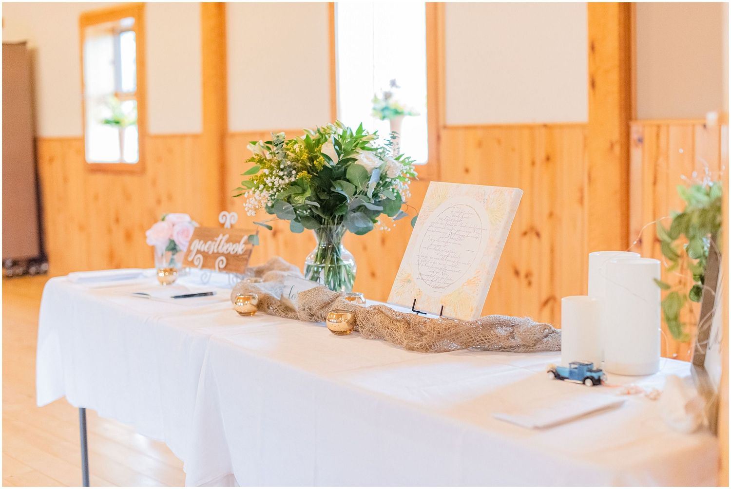 Elegant wedding welcome table with white linen, floral arrangement, and decorative driftwood.