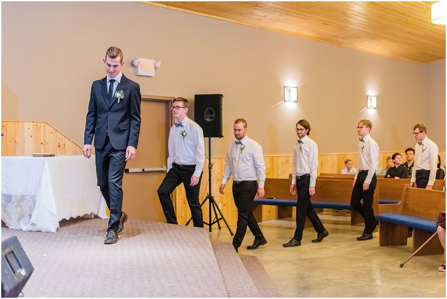 Groom leads groomsmen in white shirts down church aisle during wedding ceremony processional.