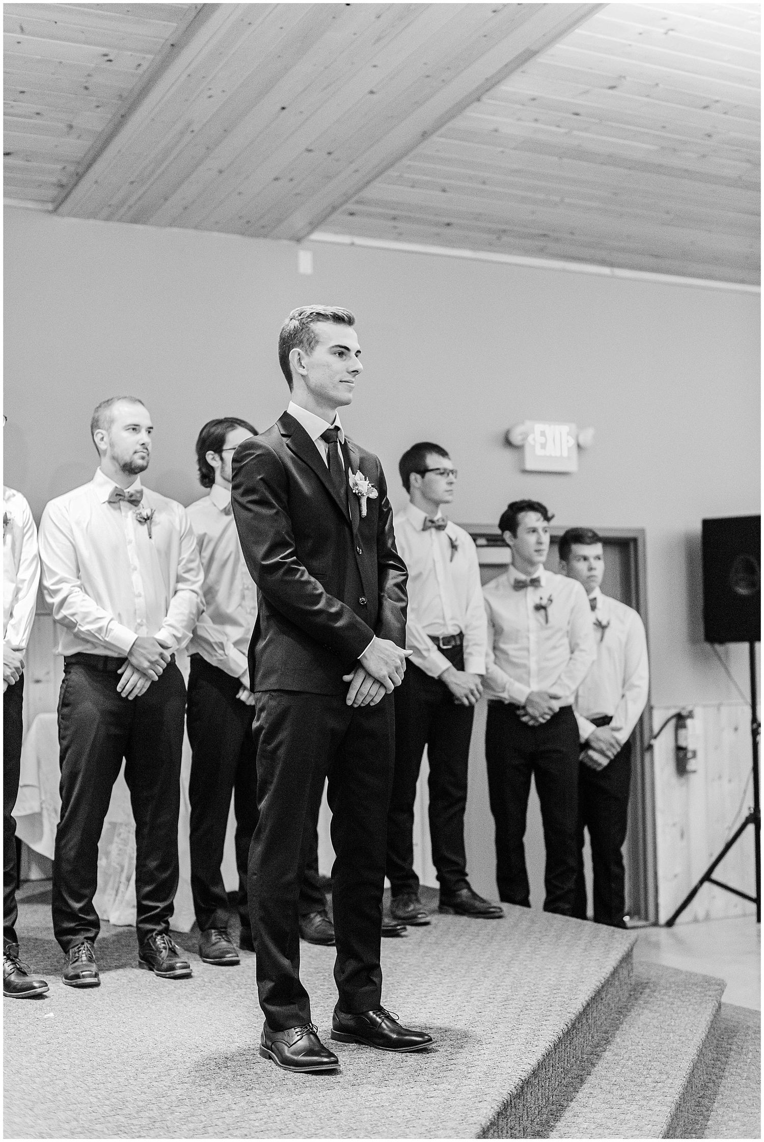 Black and white photo of groom standing at altar with groomsmen lined up behind him during wedding ceremony.