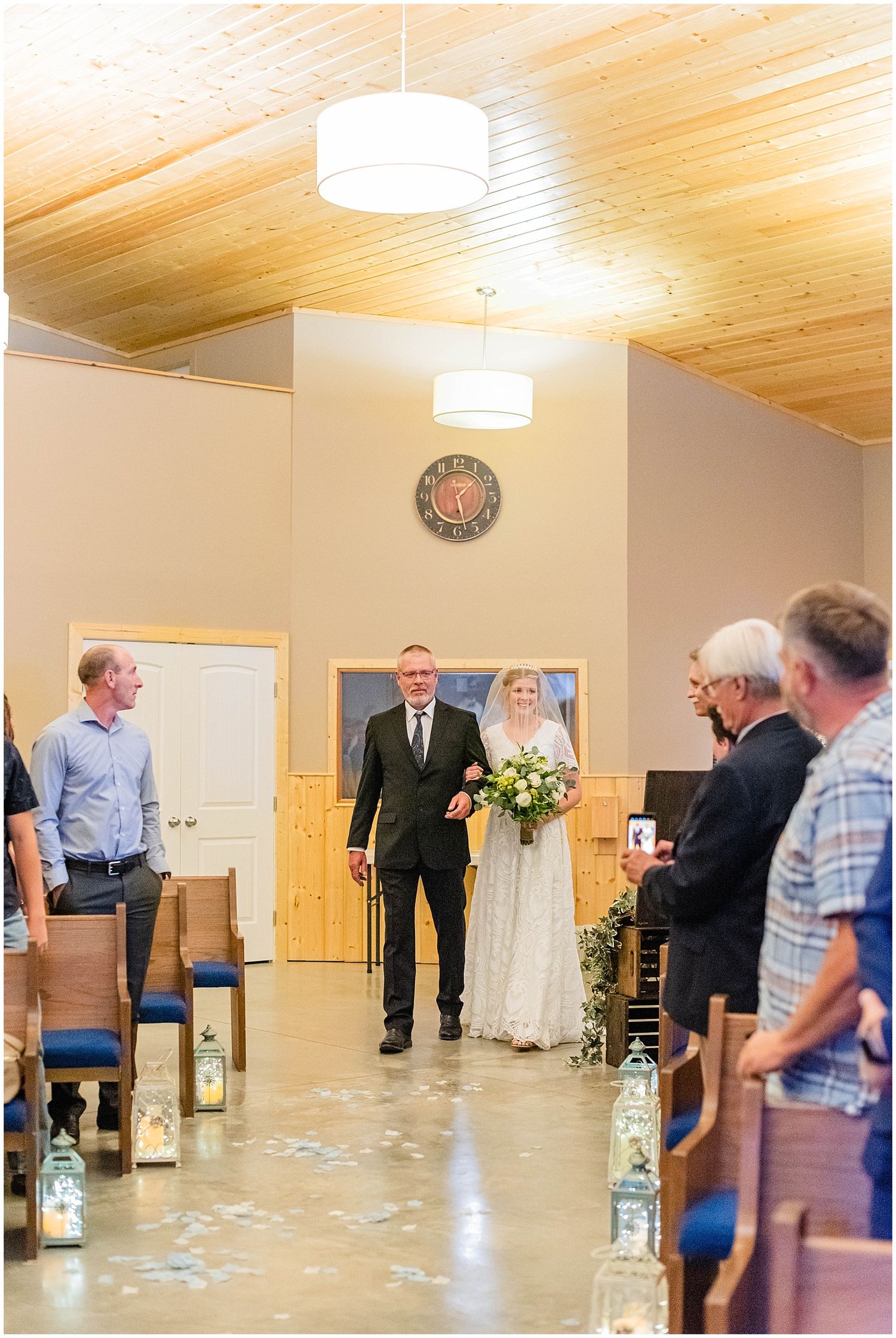Bride walks down the aisle with her father during an indoor wedding ceremony with wooden ceiling.