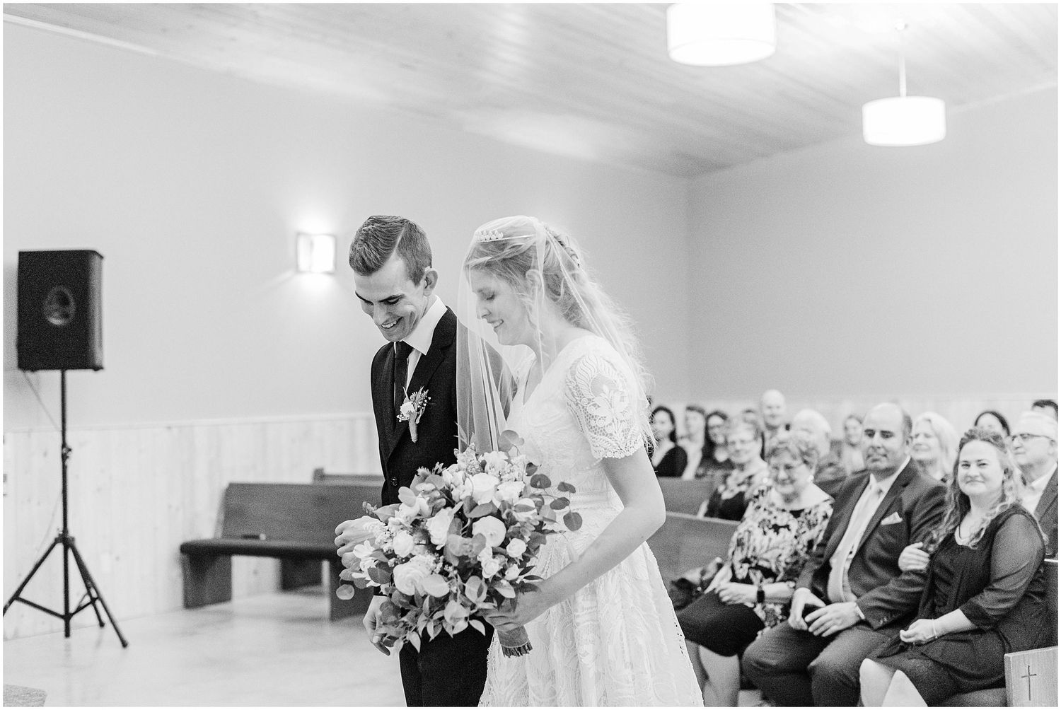 Black and white photo of bride and groom bowing heads in prayer together at wedding ceremony altar.