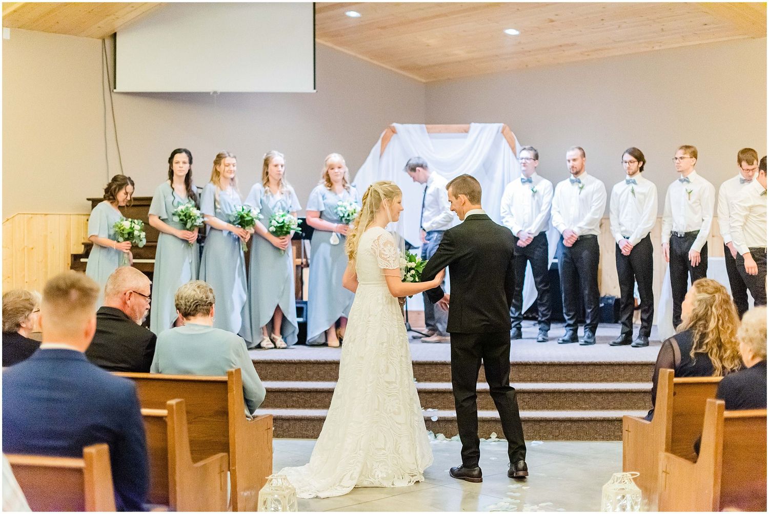 Bride and groom exchange vows at the altar surrounded by bridesmaids and groomsmen in a church.