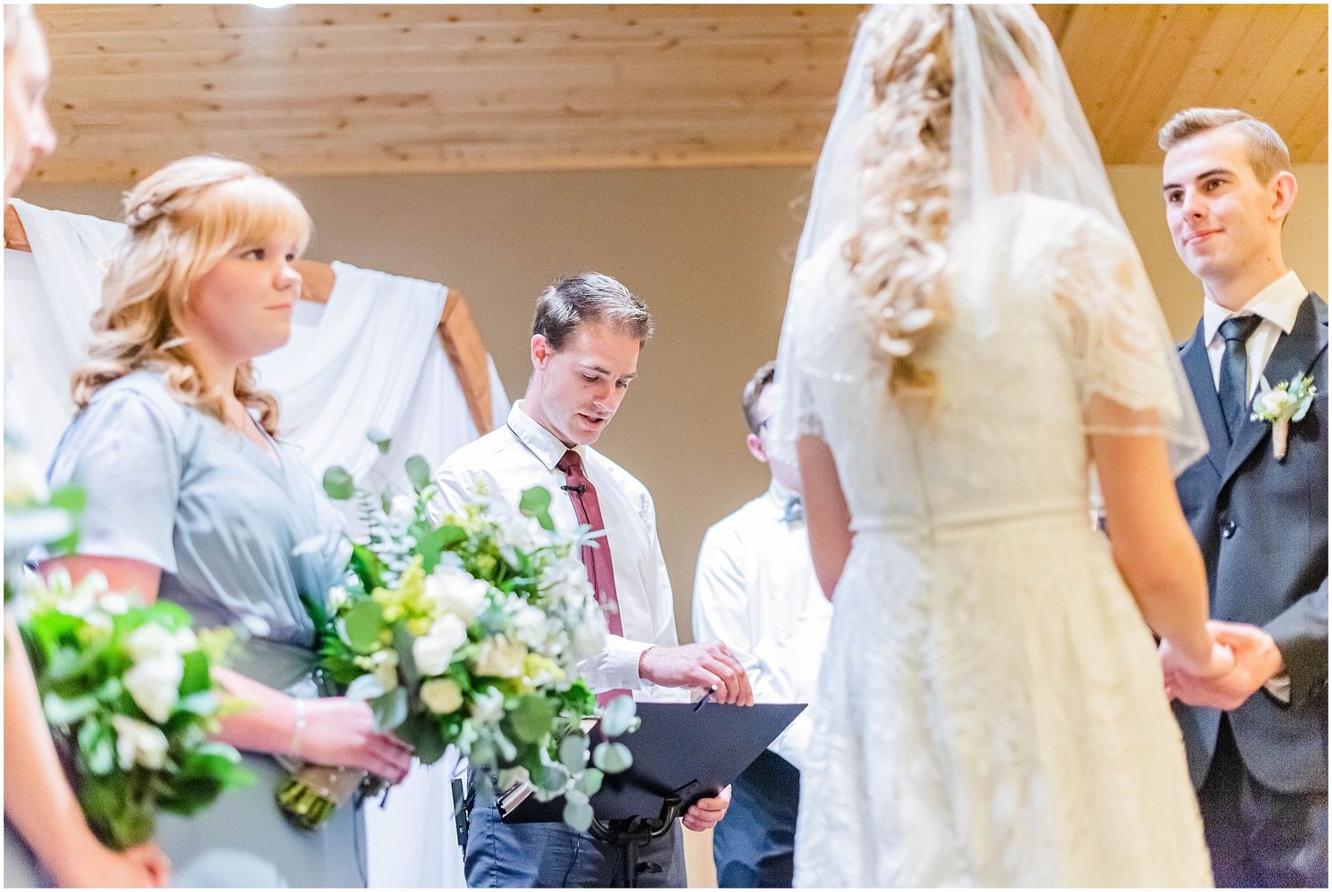 Officiant reads vows as bride and groom stand together at the altar during an indoor wedding ceremony.