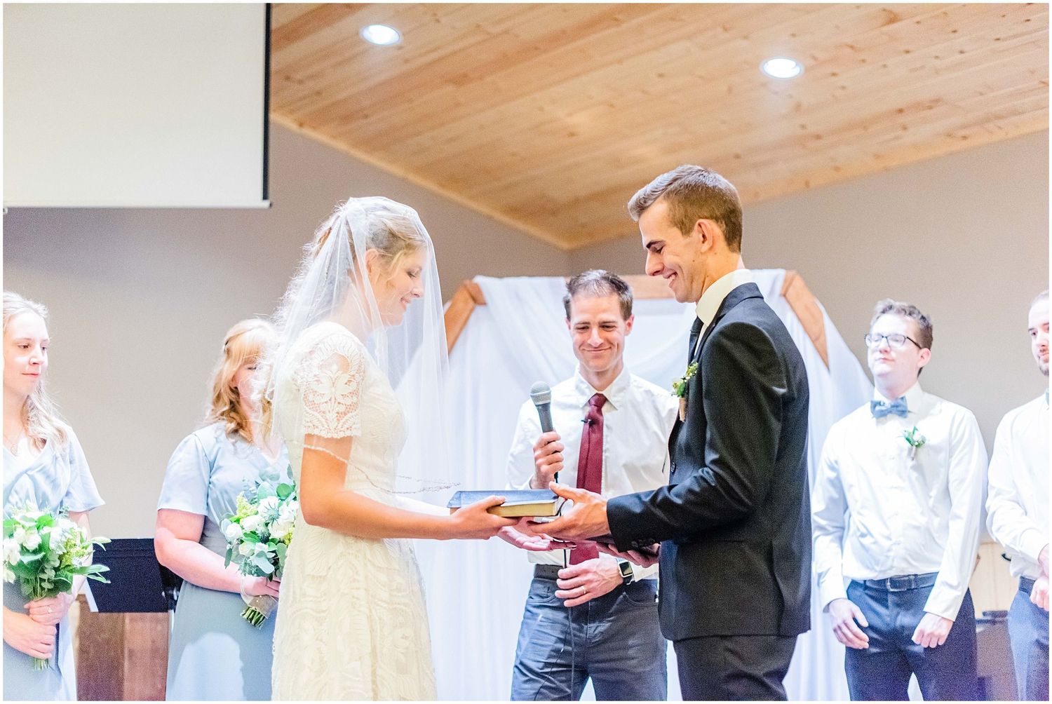Bride and groom exchange vows while officiant smiles during an intimate indoor wedding ceremony.