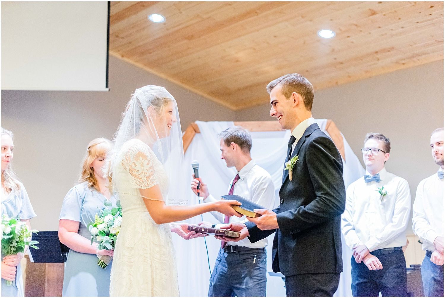Bride and groom exchange rings at the altar surrounded by bridesmaids and groomsmen in a church.