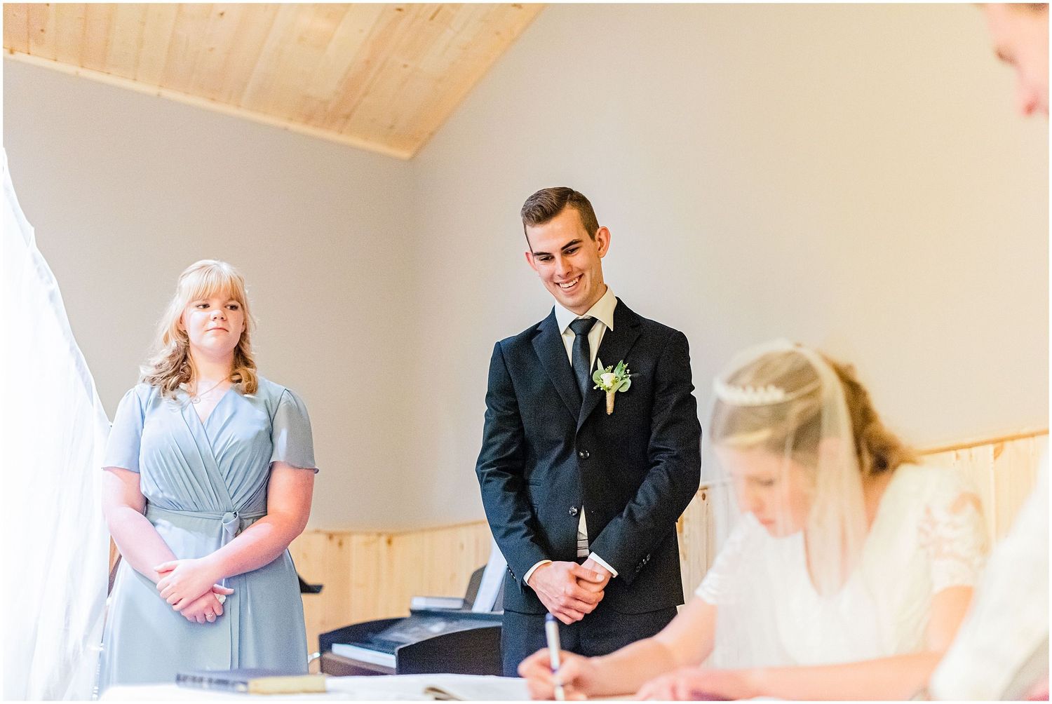 Groom watches lovingly as bride signs marriage documents during wedding ceremony signing.