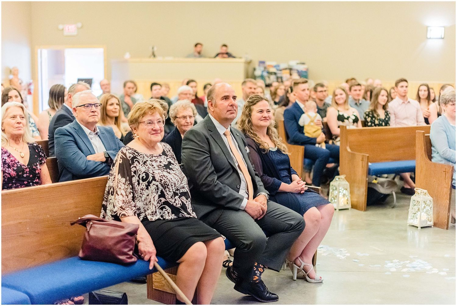 Guests seated in church pews during a wedding ceremony, dressed in formal attire.