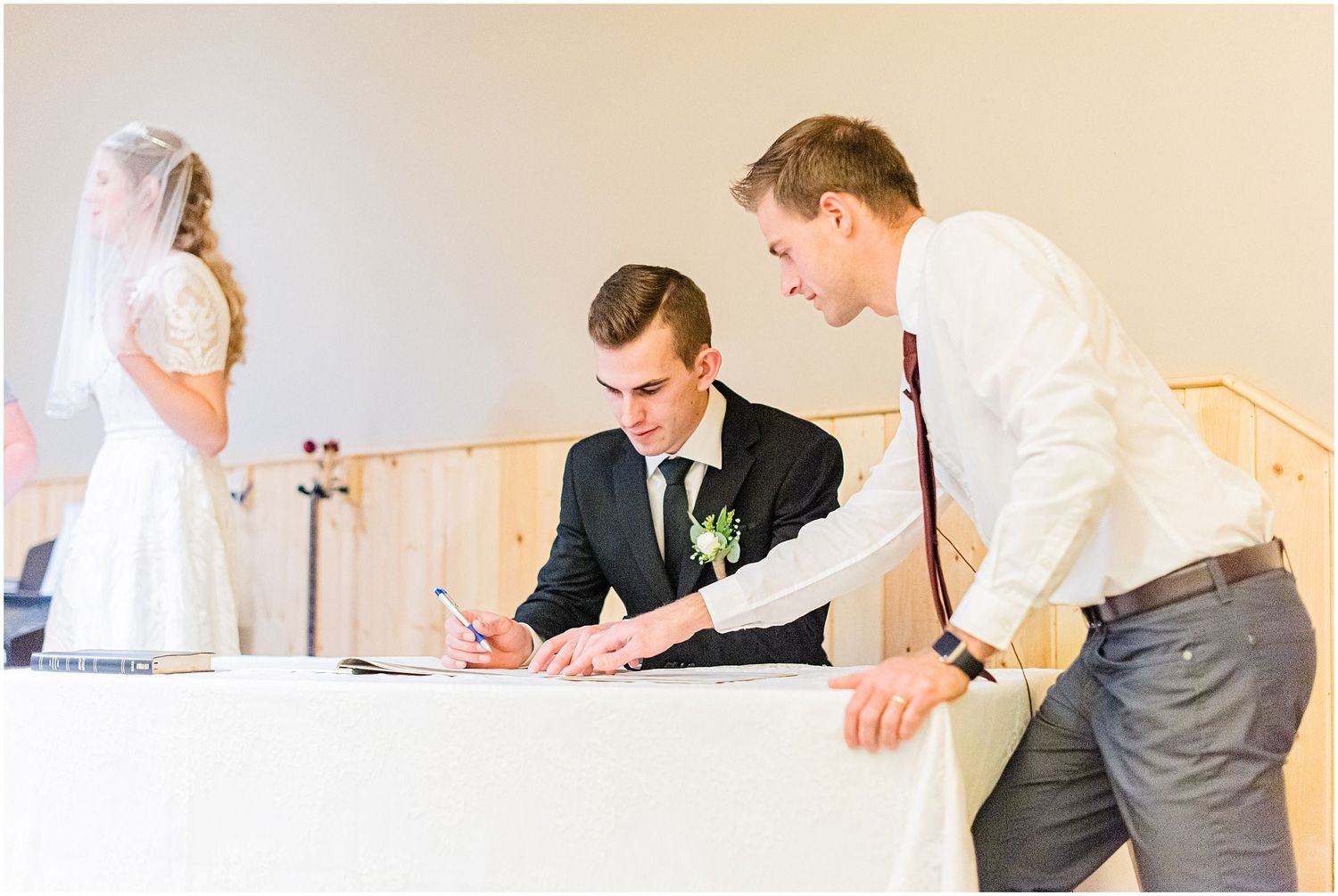 Groom signing wedding certificate at a table with a witness during the ceremony.