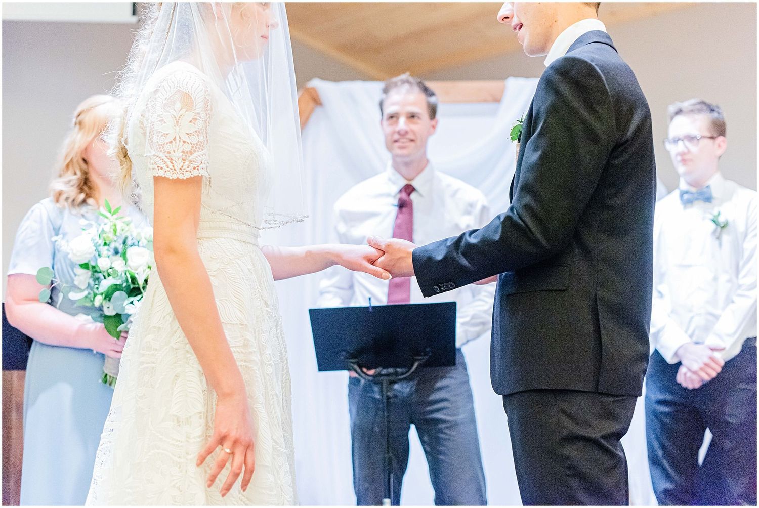 Bride and groom exchange rings at the altar as smiling officiant witnesses the ceremony.