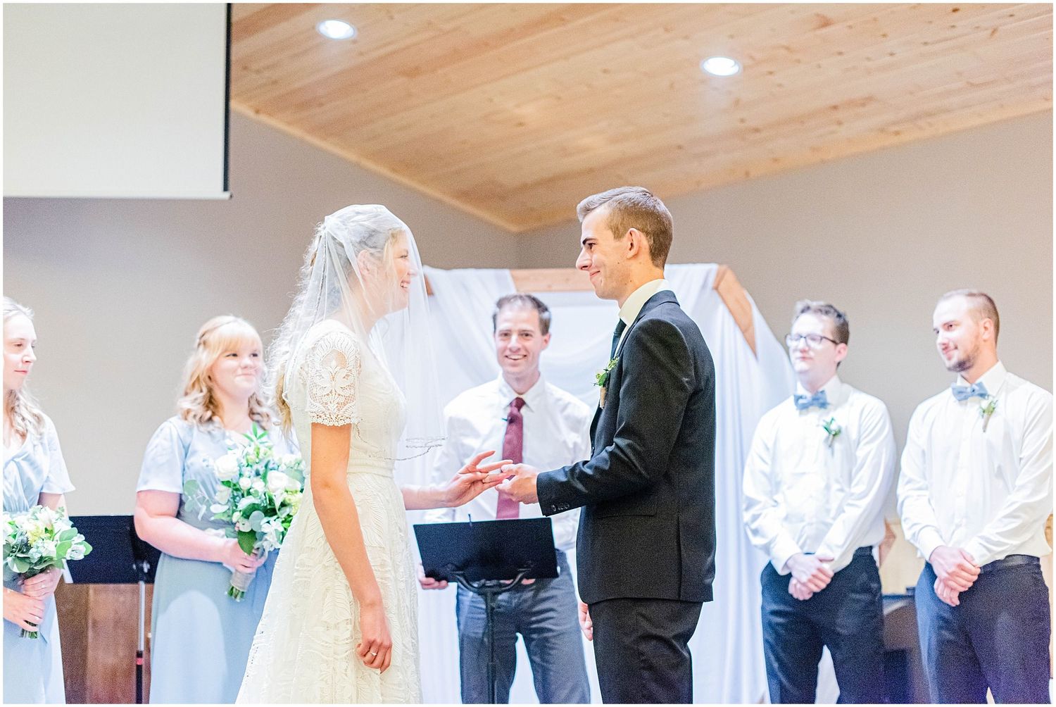 Bride and groom exchanging vows at altar surrounded by wedding party during church ceremony.