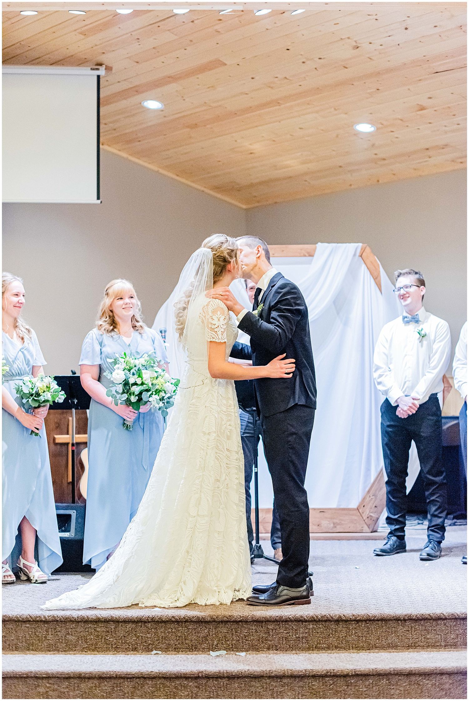 Bride and groom share first kiss at church wedding ceremony altar.