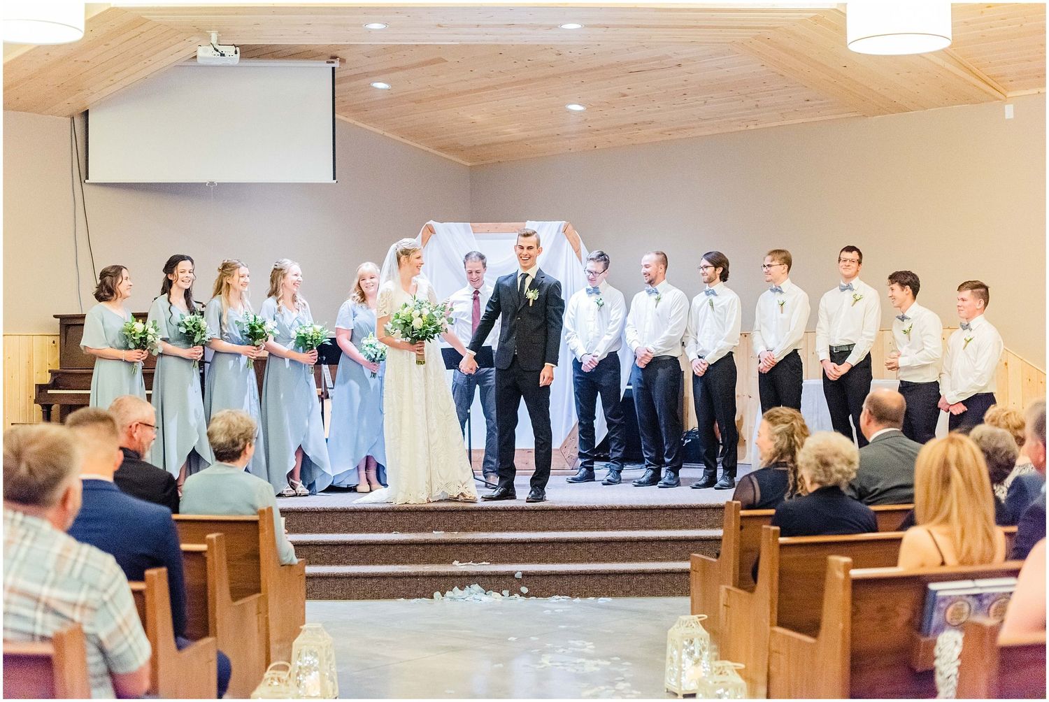 Wedding ceremony in a church with bridesmaids in blue gowns and groomsmen in black suits standing at the altar.