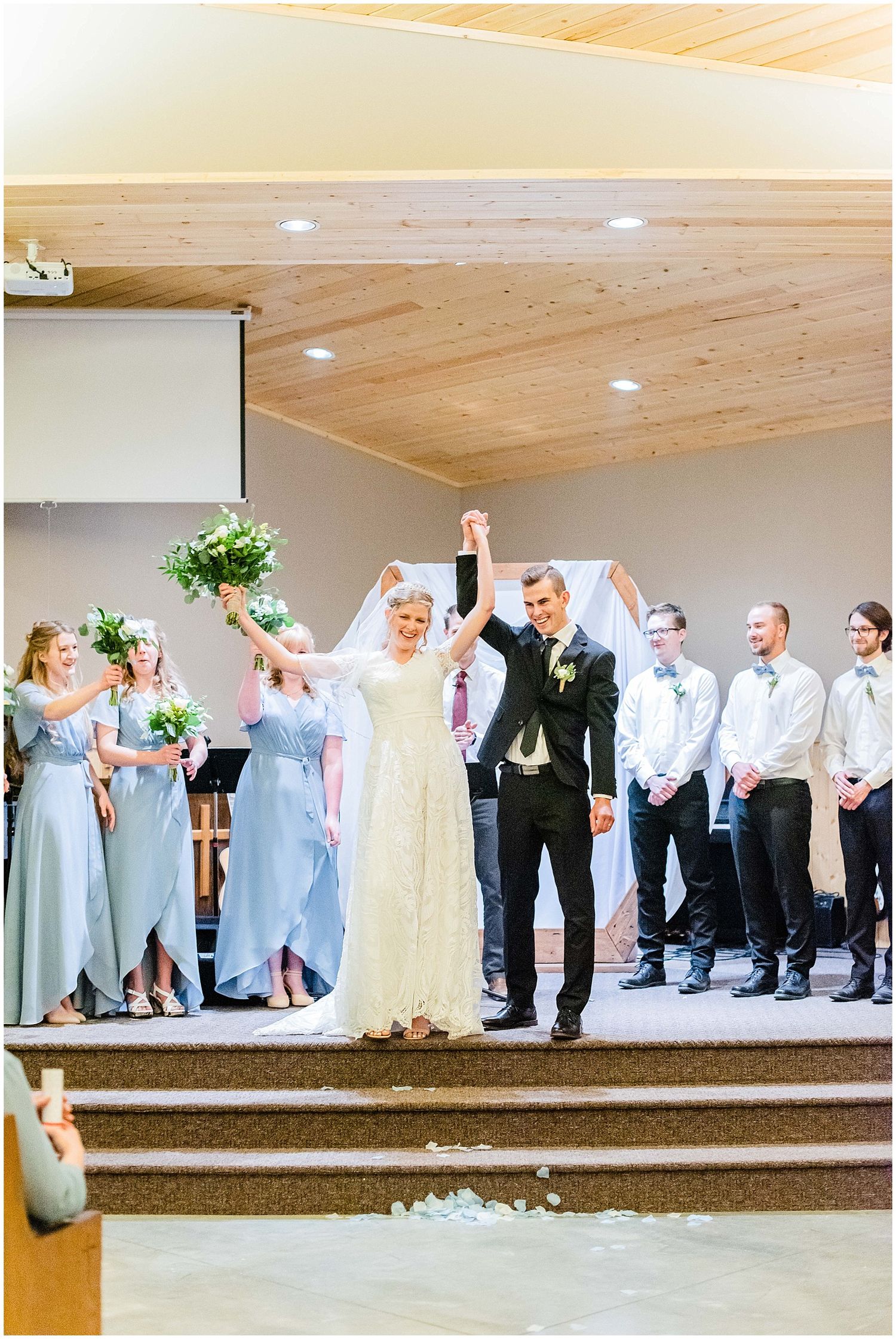 Bride and groom raise hands in celebration at church wedding ceremony.