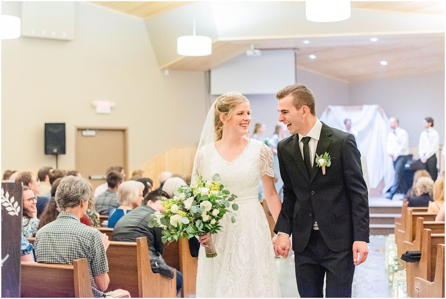 Newlyweds walk down church aisle smiling, bride holding lush floral bouquet after ceremony.