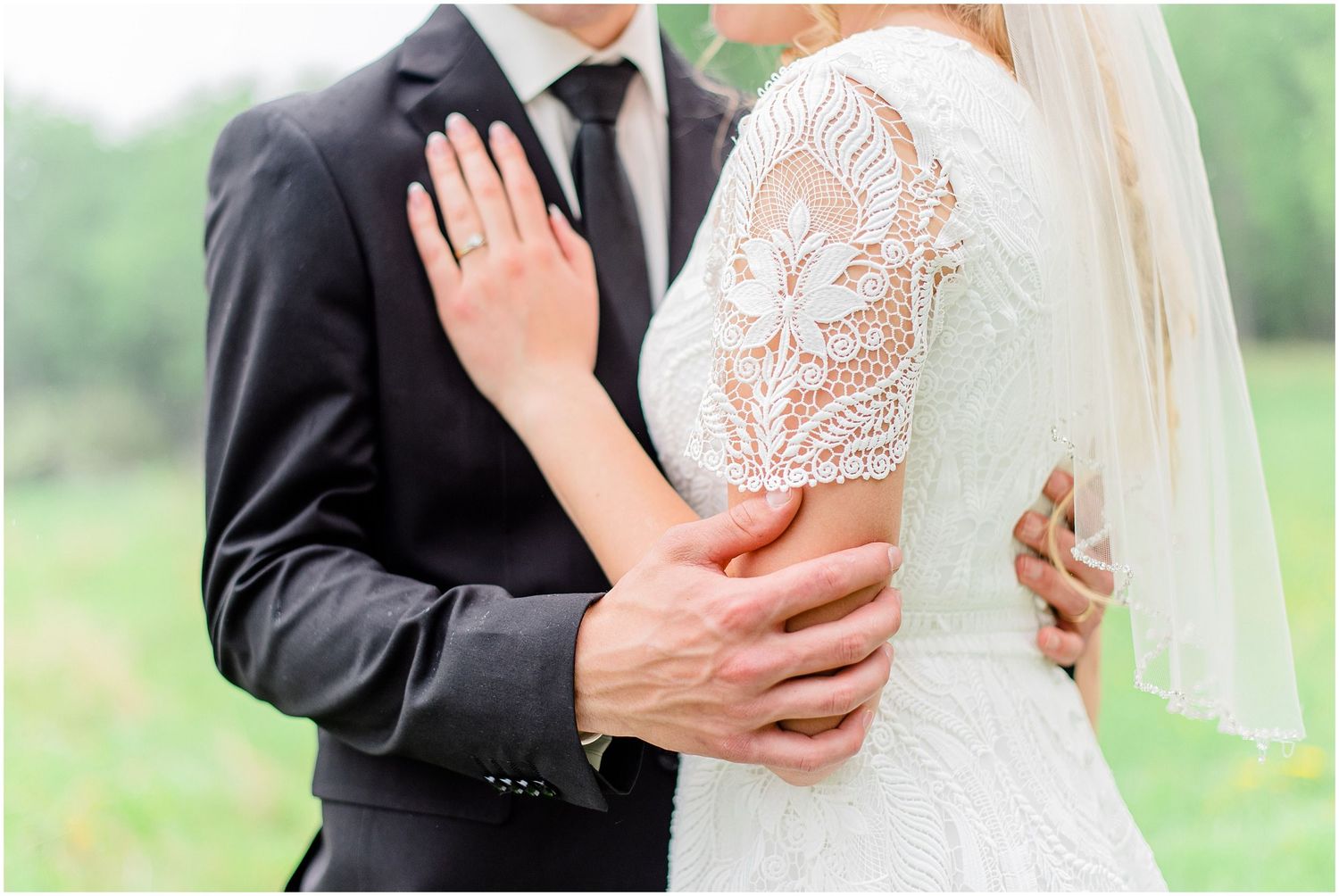 Bride and groom embrace outdoors, showcasing lace wedding dress and ring.