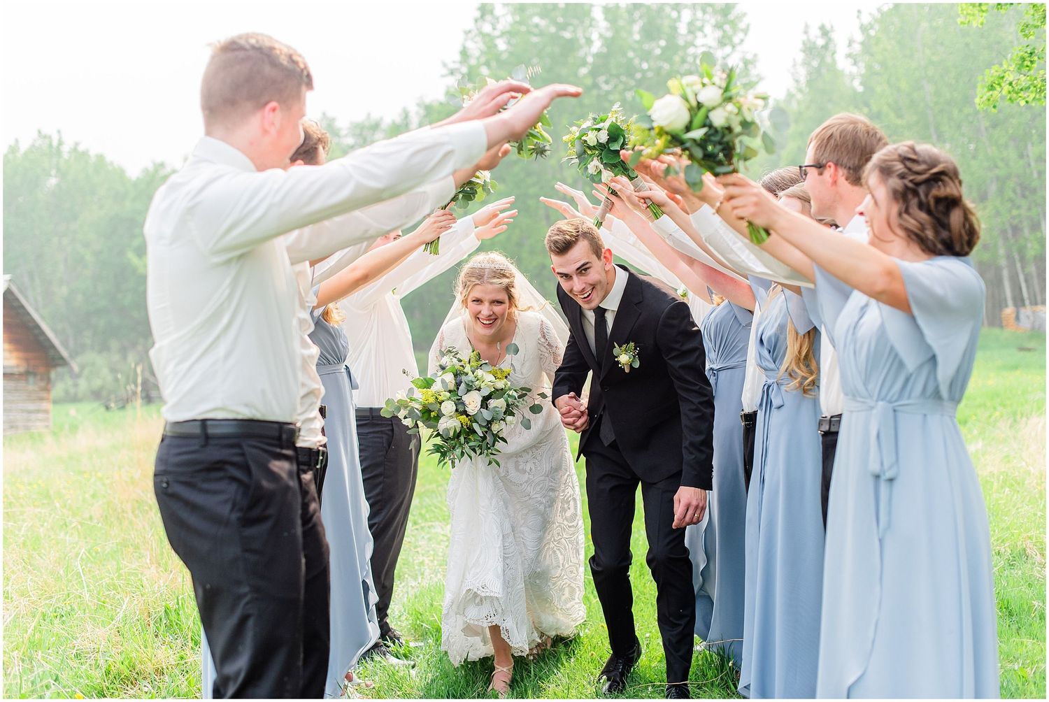 Bride and groom walk through an arch of raised bouquets held by bridesmaids in blue dresses and groomsmen.