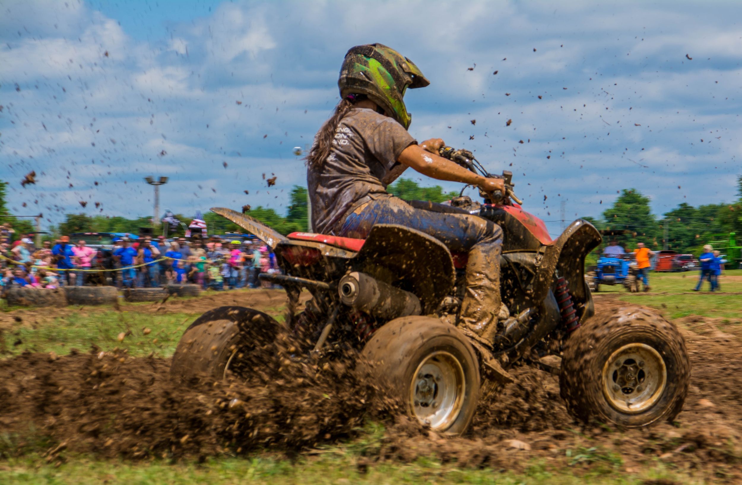 ATV rider racing through mud at rural outdoor event Northwest Arkansas with crowd watching